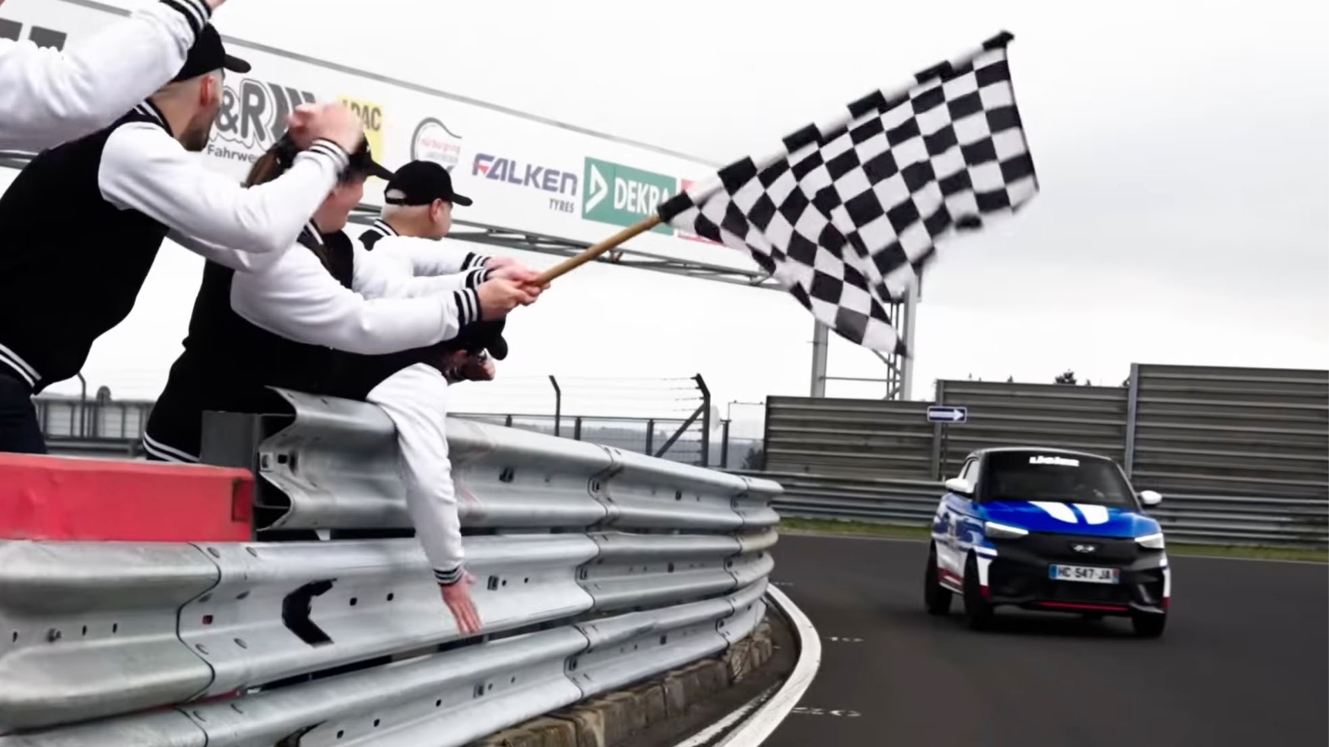 A race car crosses the finish line as someone waves a checkered flag.