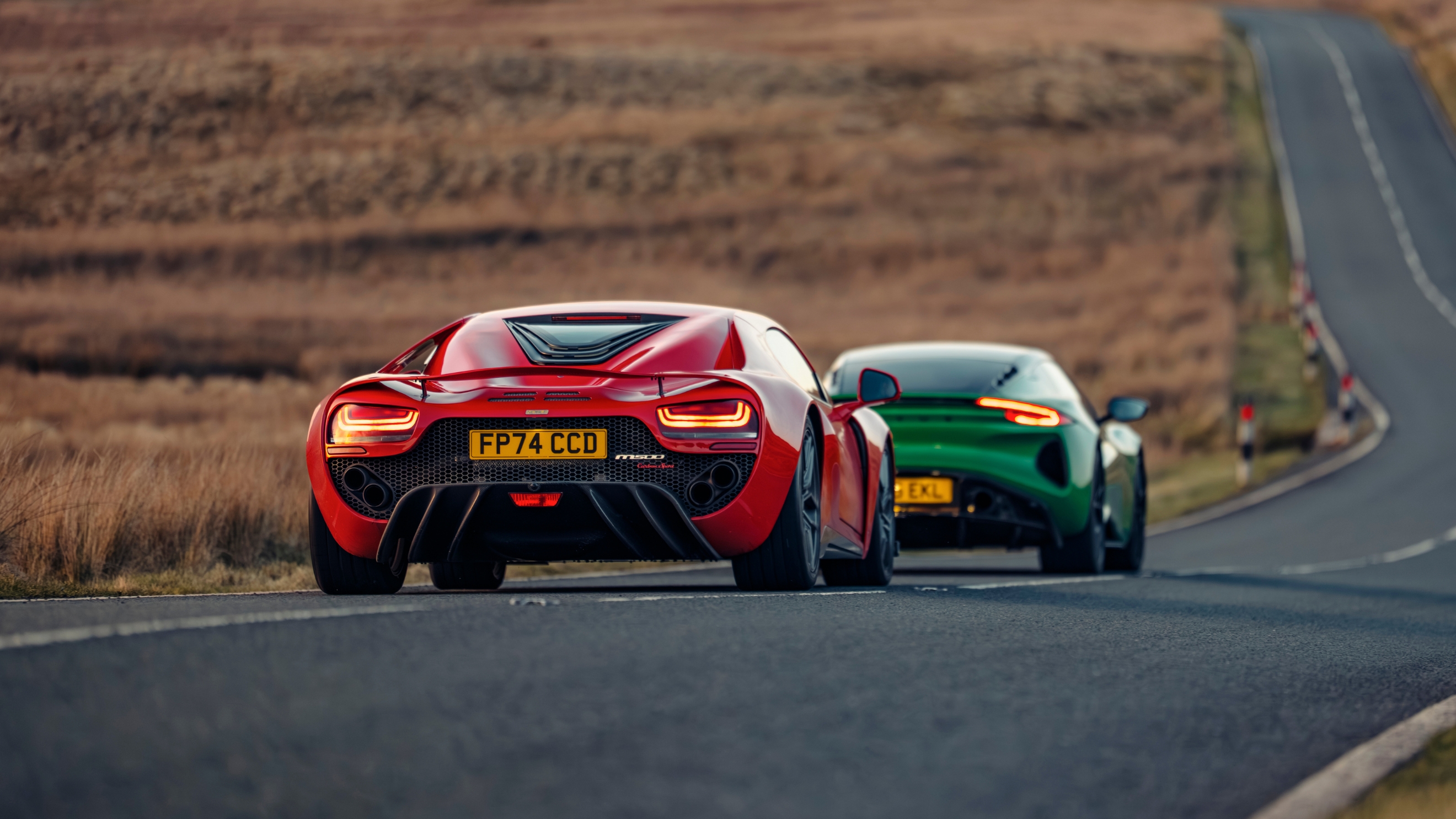 Noble M500 and Lotus Emira driving on a road pictured from the back